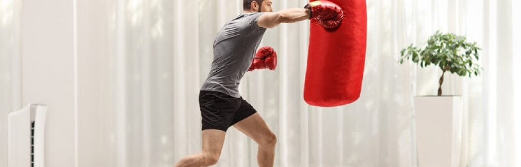 Man exercising punching bag with boxing gloves at home